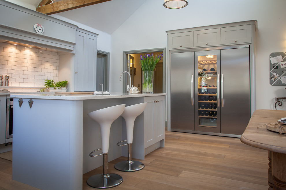 Large trendy u-shaped medium tone wood floor eat-in kitchen photo in Hertfordshire with a farmhouse sink, shaker cabinets, gray cabinets, quartzite countertops, white backsplash, ceramic backsplash, stainless steel appliances and an island