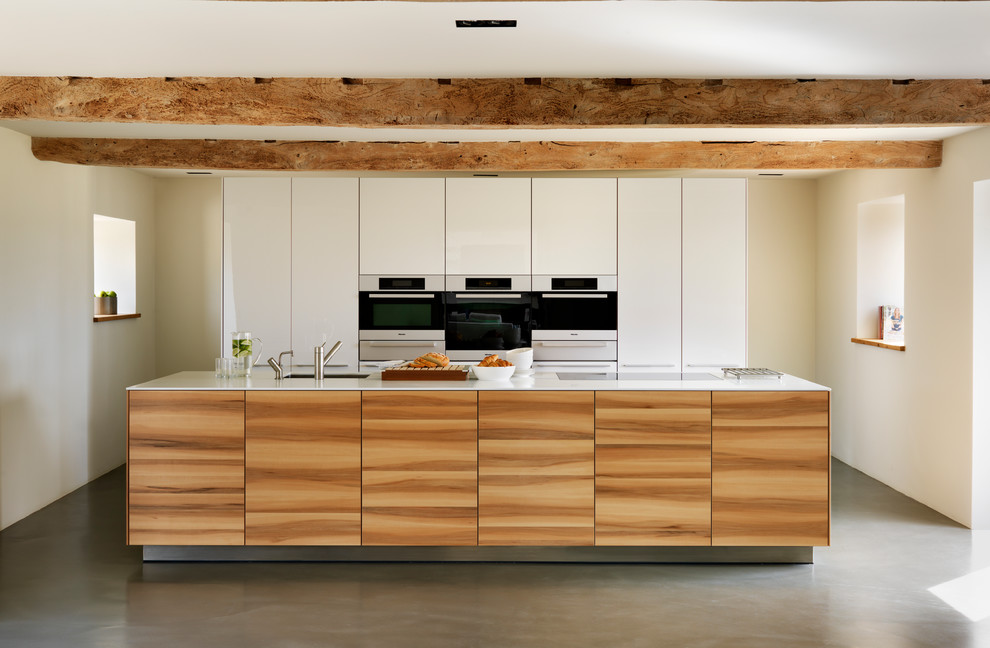 Moderne Küche mit flächenbündigen Schrankfronten, hellbraunen Holzschränken, Küchengeräten aus Edelstahl, Betonboden und Kücheninsel in Oxfordshire