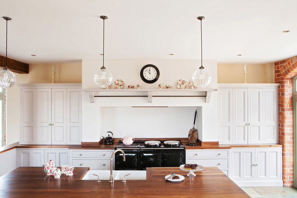 Idéer för ett lantligt kök, med en rustik diskho, luckor med infälld panel, vita skåp, träbänkskiva, vitt stänkskydd, svarta vitvaror och en köksö
