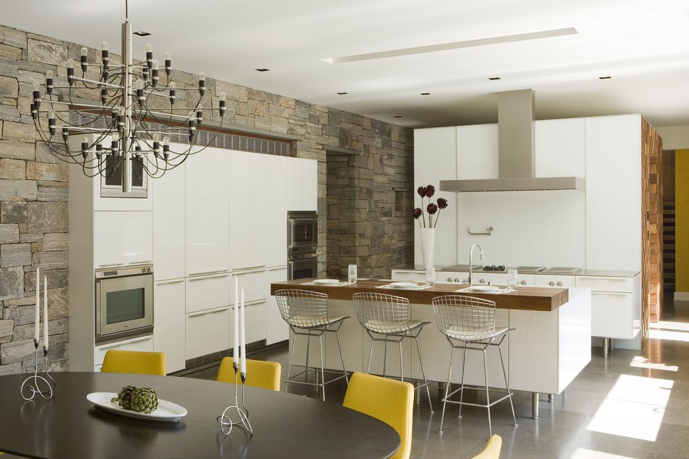 This is an example of a large contemporary l-shaped kitchen/diner in New York with flat-panel cabinets, white cabinets, stainless steel worktops, white splashback, integrated appliances, a submerged sink, concrete flooring and an island.