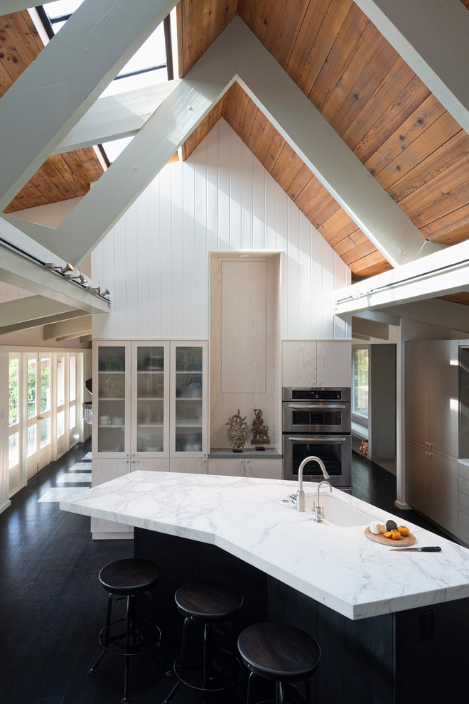 Cette image montre une cuisine design en bois clair avec un évier encastré, un placard à porte vitrée et un électroménager en acier inoxydable.