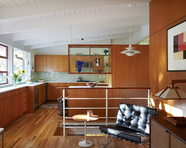 Idée de décoration pour une petite cuisine américaine vintage en L et bois brun avec un placard à porte plane, une crédence verte, une crédence en céramique et un sol en bois brun.