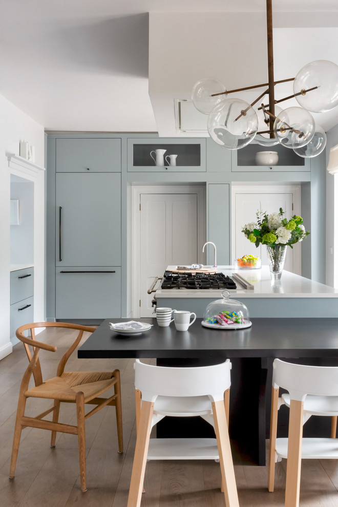 Traditional kitchen/diner in London with a double-bowl sink, flat-panel cabinets, blue cabinets, composite countertops, mirror splashback, stainless steel appliances, medium hardwood flooring, a breakfast bar, brown floors and white worktops.