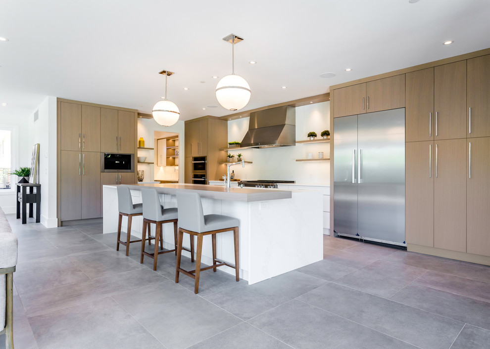 Large modern l-shaped open plan kitchen in Vancouver with a submerged sink, flat-panel cabinets, medium wood cabinets, quartz worktops, white splashback, stone slab splashback, stainless steel appliances, cement flooring, an island, grey floors and white worktops.