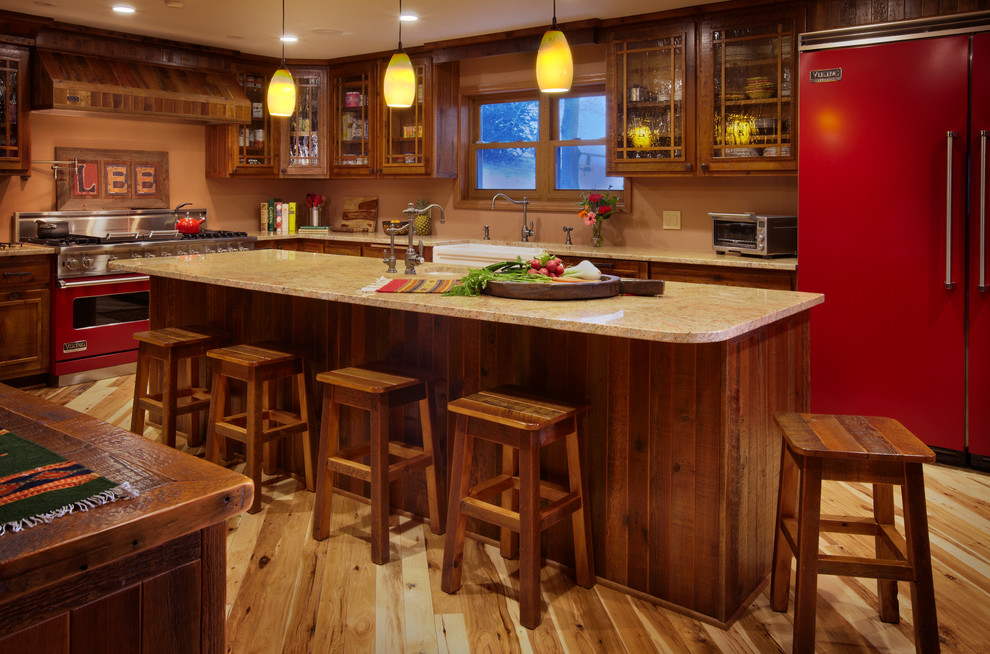 Cette image montre une cuisine américaine chalet en bois foncé et U avec un évier de ferme, un placard à porte vitrée, un électroménager de couleur, un plan de travail en granite, parquet clair et îlot.