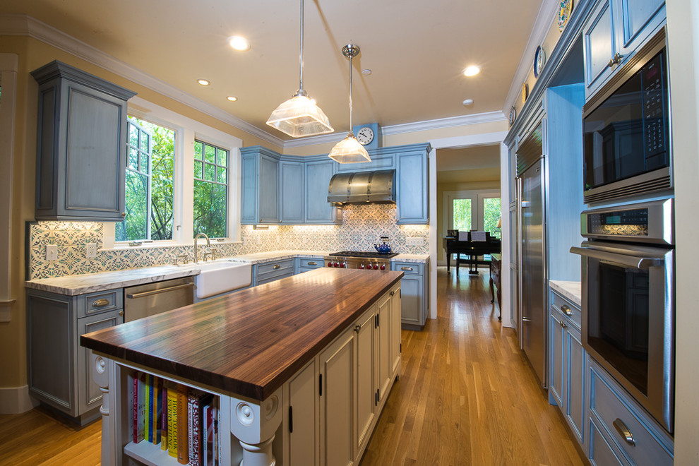 Large farmhouse u-shaped medium tone wood floor and brown floor enclosed kitchen photo in San Francisco with a farmhouse sink, beaded inset cabinets, blue cabinets, wood countertops, multicolored backsplash, mosaic tile backsplash, stainless steel appliances and an island