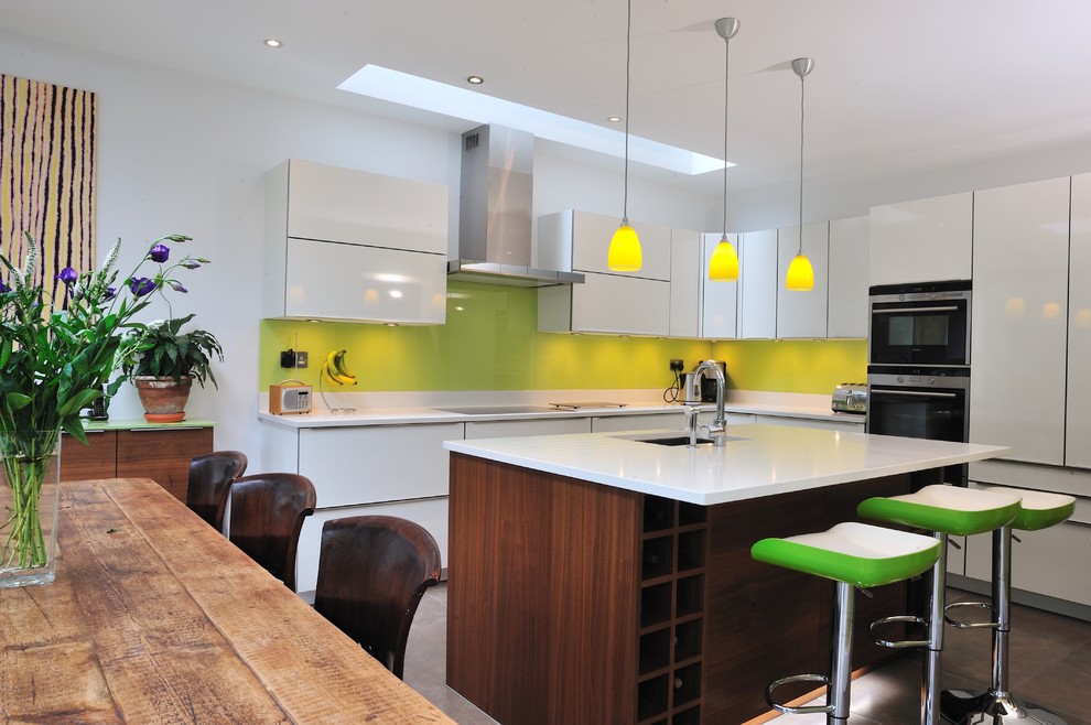 Inspiration for a medium sized modern kitchen/diner in Surrey with a submerged sink, flat-panel cabinets, white cabinets, green splashback, glass sheet splashback, stainless steel appliances, ceramic flooring and an island.