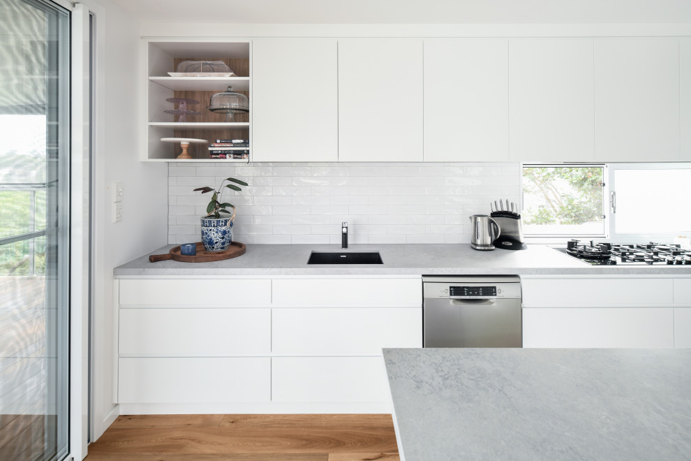 Bild på ett mellanstort funkis grå grått kök, med en undermonterad diskho, släta luckor, vita skåp, bänkskiva i kvarts, vitt stänkskydd, stänkskydd i keramik, rostfria vitvaror, mellanmörkt trägolv, en köksö och brunt golv