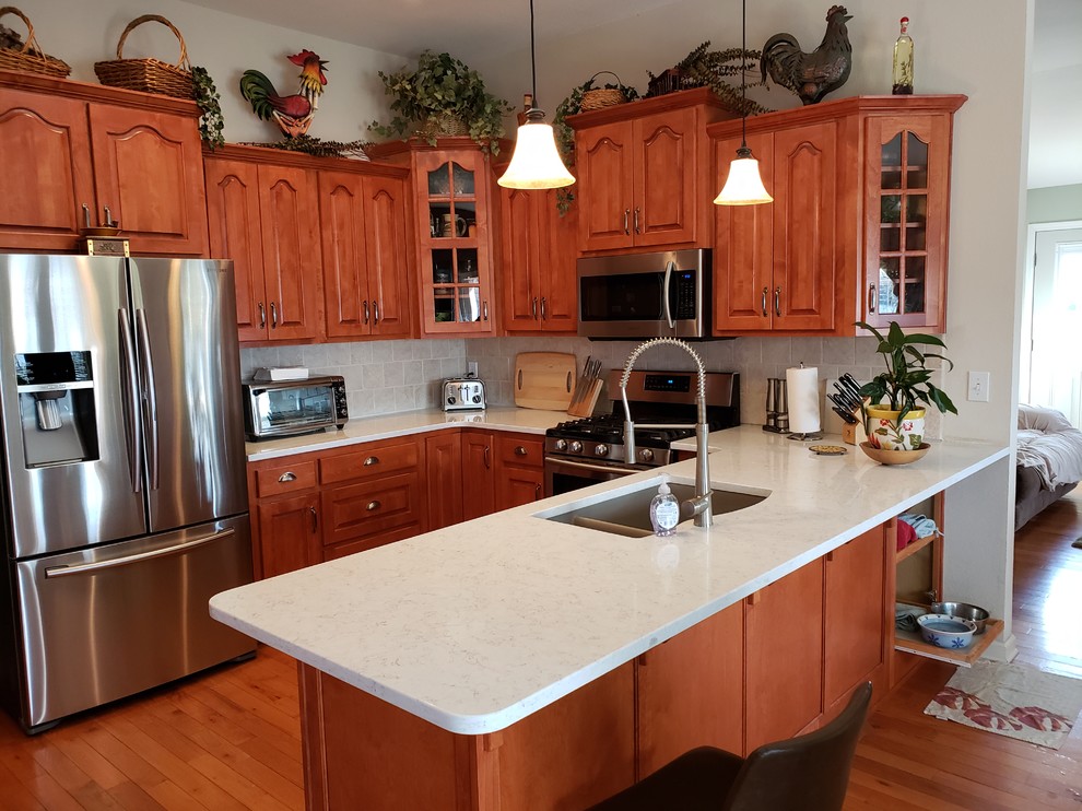Exempel på ett mellanstort klassiskt gul gult kök, med en undermonterad diskho, luckor med upphöjd panel, skåp i mellenmörkt trä, bänkskiva i kvartsit, vitt stänkskydd, stänkskydd i porslinskakel, rostfria vitvaror, ljust trägolv, en halv köksö och brunt golv