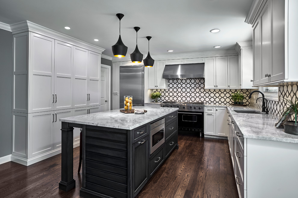 Klassisk inredning av ett grå grått u-kök, med en undermonterad diskho, skåp i shakerstil, vita skåp, flerfärgad stänkskydd, rostfria vitvaror, mörkt trägolv, en köksö och brunt golv