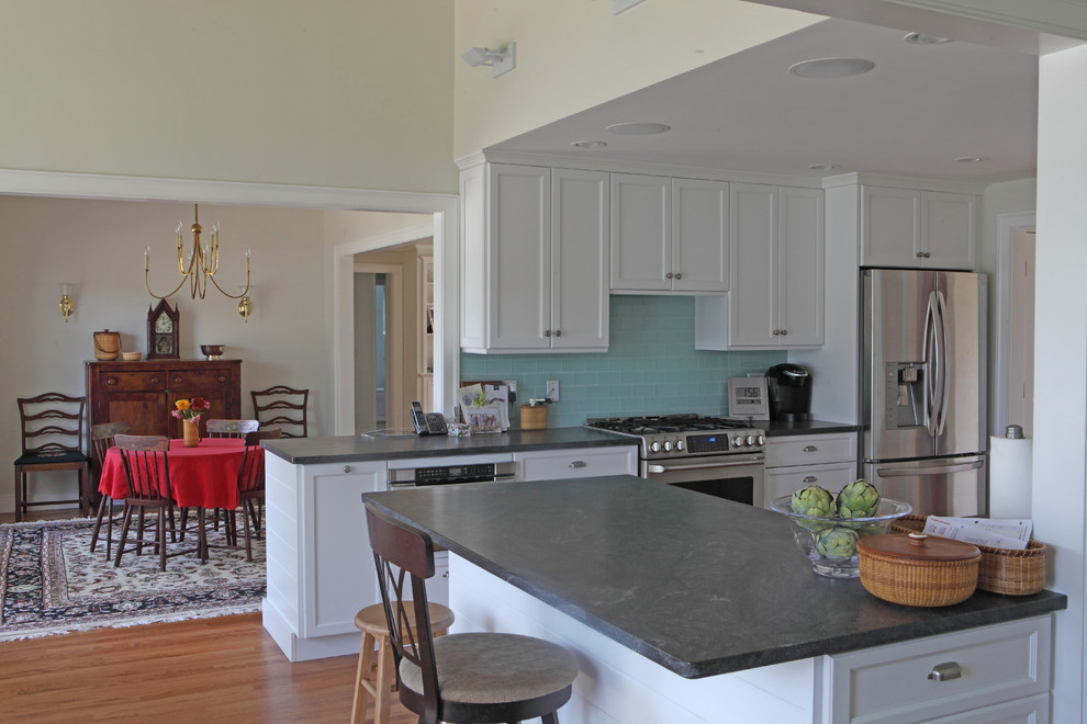 Maritim inredning av ett stort kök och matrum, med en undermonterad diskho, luckor med upphöjd panel, granitbänkskiva, blått stänkskydd, stänkskydd i glaskakel, rostfria vitvaror, ljust trägolv, en köksö och vita skåp