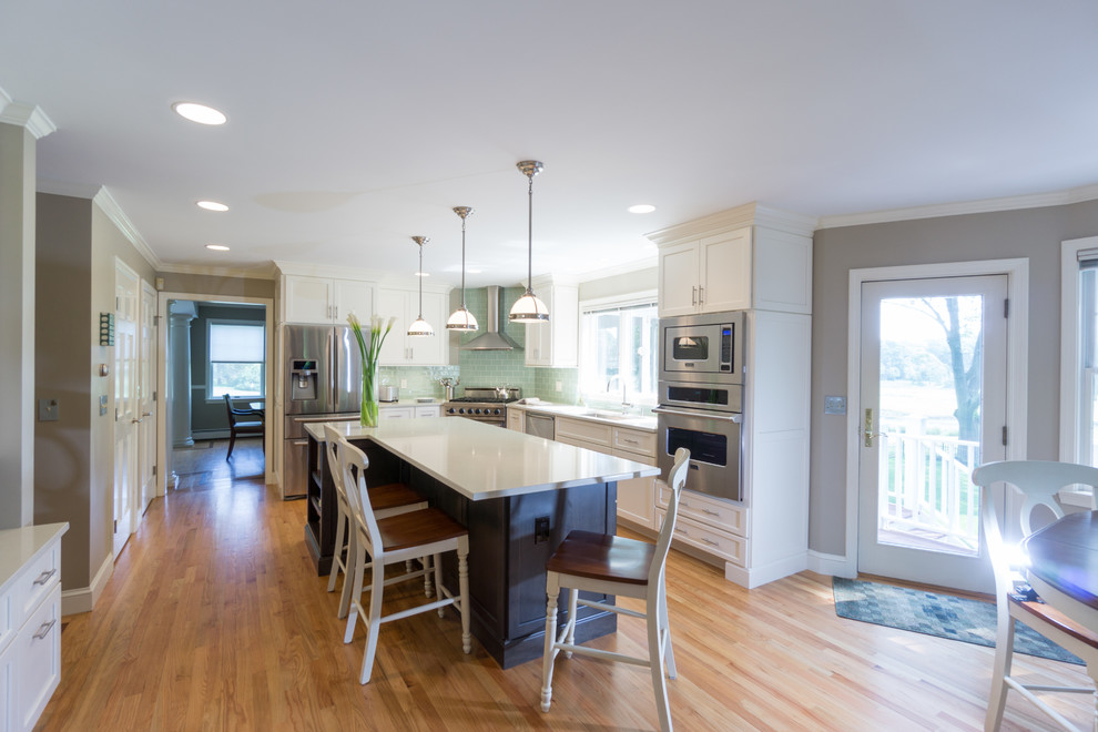 Large classic l-shaped kitchen/diner in Providence with an island, shaker cabinets, white cabinets, engineered stone countertops, green splashback, glass tiled splashback, stainless steel appliances, a submerged sink and light hardwood flooring.