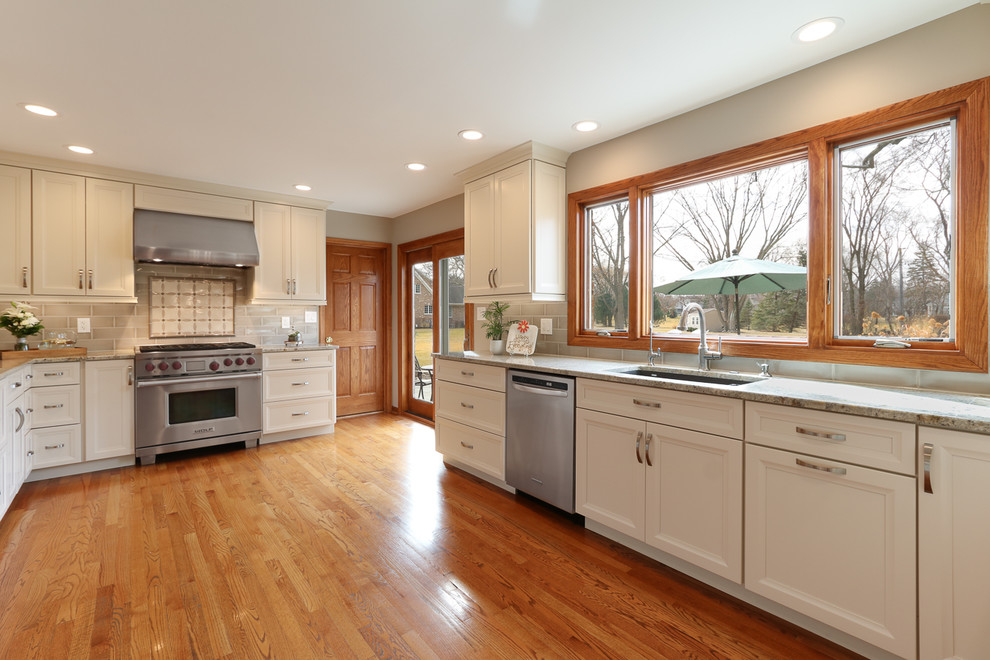 Inredning av ett klassiskt stort kök, med en enkel diskho, luckor med infälld panel, vita skåp, granitbänkskiva, grått stänkskydd, stänkskydd i keramik, rostfria vitvaror, mellanmörkt trägolv, en halv köksö och brunt golv