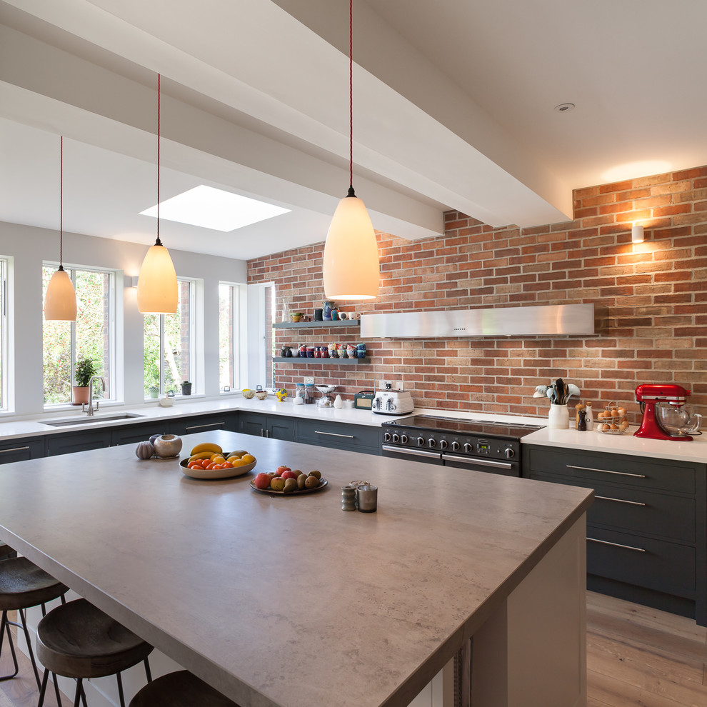 Large contemporary l-shaped kitchen/diner in London with a built-in sink, flat-panel cabinets, grey cabinets, concrete worktops, integrated appliances, medium hardwood flooring and a breakfast bar.