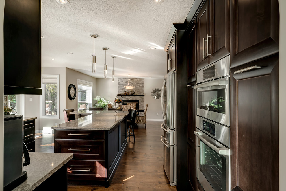 Mittelgroße Retro Wohnküche in U-Form mit Unterbauwaschbecken, Schrankfronten im Shaker-Stil, dunklen Holzschränken, Granit-Arbeitsplatte, bunter Rückwand, Küchengeräten aus Edelstahl, braunem Holzboden und Kücheninsel in Vancouver