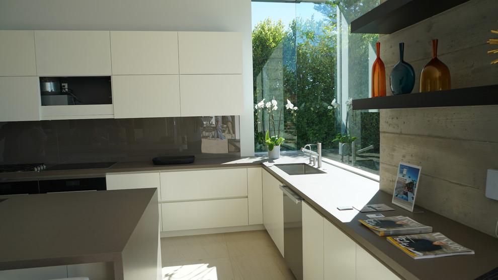 Large beach style galley kitchen/diner in San Francisco with a submerged sink, glass-front cabinets, white cabinets, quartz worktops, grey splashback, glass sheet splashback, black appliances, cement flooring, multiple islands, white floors and grey worktops.