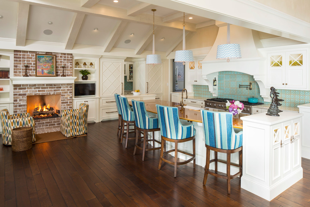 Example of a beach style dark wood floor and brown floor open concept kitchen design in Minneapolis with glass-front cabinets, white cabinets, green backsplash, stainless steel appliances, an island and gray countertops