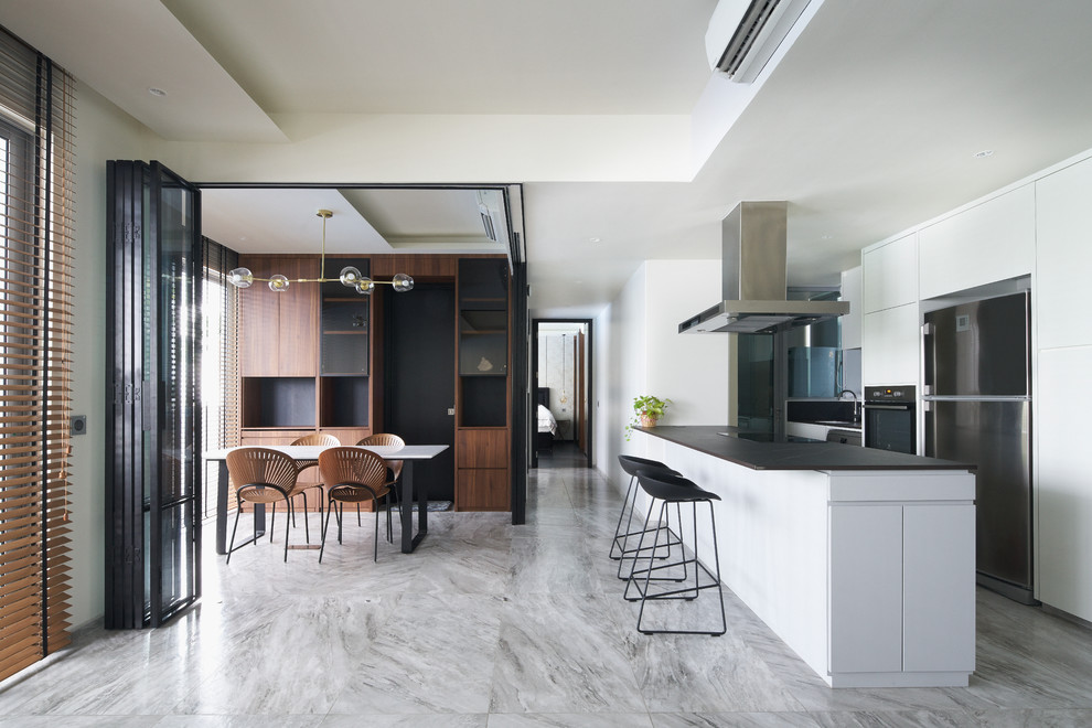 Zweizeilige Moderne Küche mit flächenbündigen Schrankfronten, weißen Schränken, Küchengeräten aus Edelstahl, Kücheninsel, grauem Boden und schwarzer Arbeitsplatte