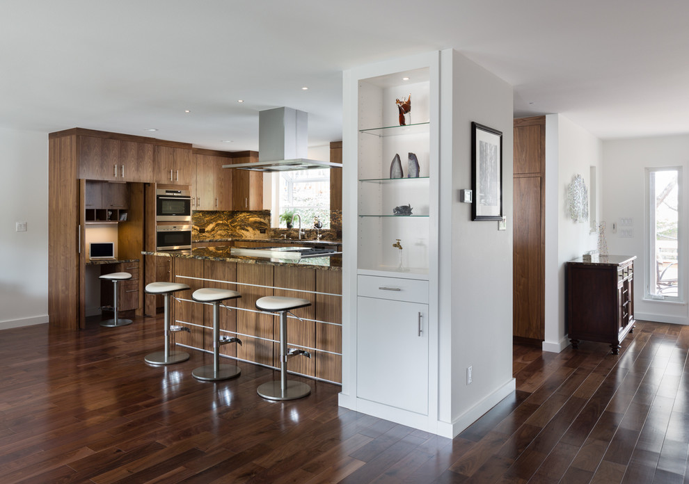 Photo of a contemporary l-shaped kitchen/diner in Austin with flat-panel cabinets, medium wood cabinets, granite worktops, stainless steel appliances, a submerged sink, multi-coloured splashback, stone slab splashback, medium hardwood flooring and a breakfast bar.