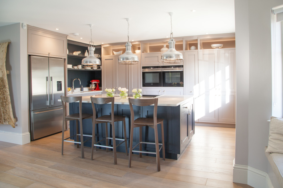 Example of a transitional l-shaped light wood floor and beige floor kitchen design in Surrey with an undermount sink, shaker cabinets, quartzite countertops, stainless steel appliances, an island and gray cabinets