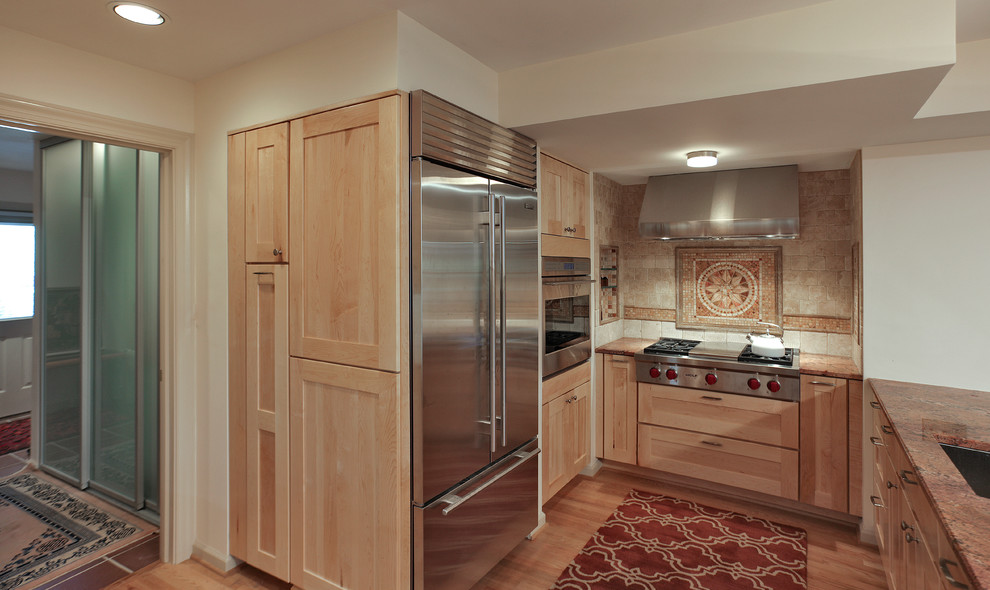 Modelo de cocina comedor contemporánea con fregadero bajoencimera, armarios estilo shaker, puertas de armario de madera clara, encimera de granito, salpicadero rojo y electrodomésticos de acero inoxidable