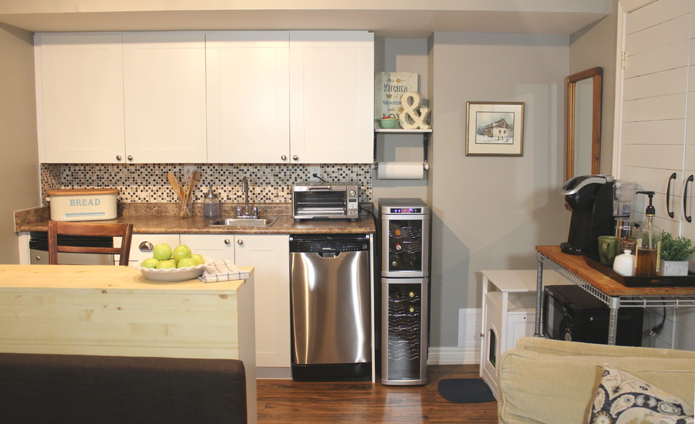 Example of a small farmhouse single-wall laminate floor and brown floor eat-in kitchen design in Toronto with a single-bowl sink, shaker cabinets, white cabinets, laminate countertops, brown backsplash, ceramic backsplash, stainless steel appliances and an island