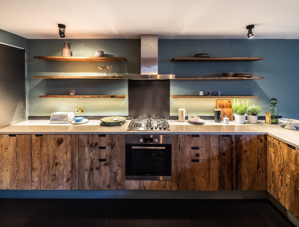 Cette photo montre une cuisine tendance en L et bois clair de taille moyenne avec un placard à porte plane, un plan de travail en quartz, une crédence bleue, un électroménager en acier inoxydable et un sol noir.