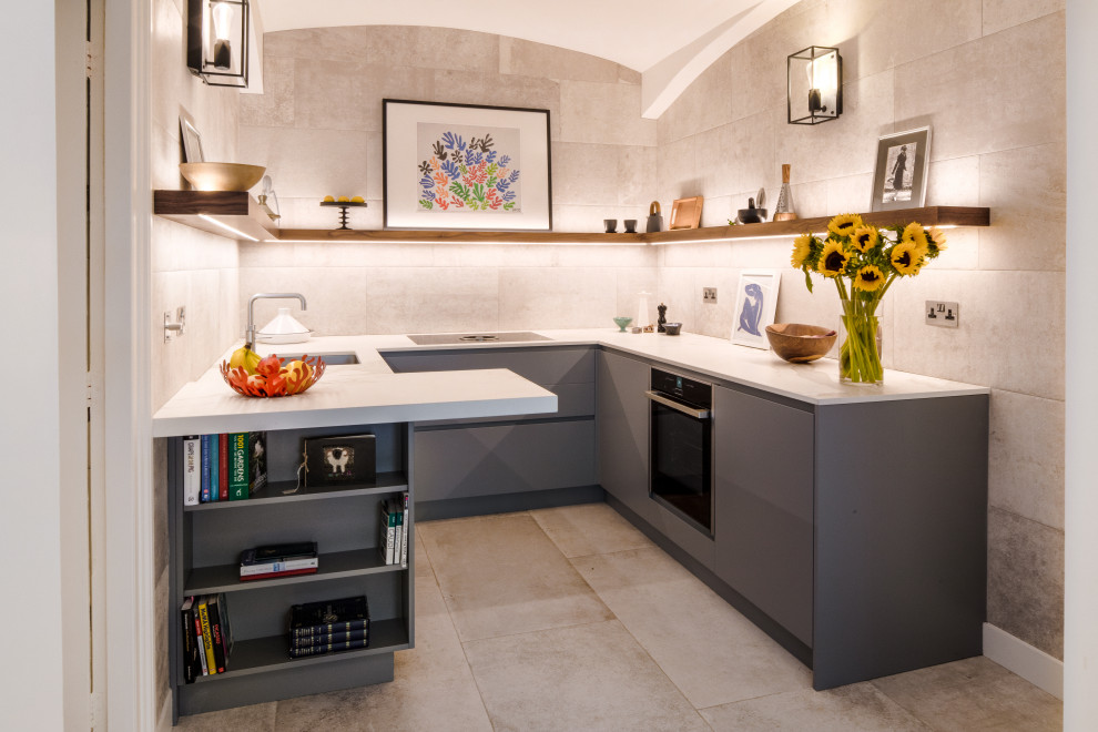 This is an example of a small contemporary enclosed kitchen in London with an integrated sink, flat-panel cabinets, grey cabinets, engineered stone countertops, grey splashback, black appliances, ceramic flooring and white worktops.