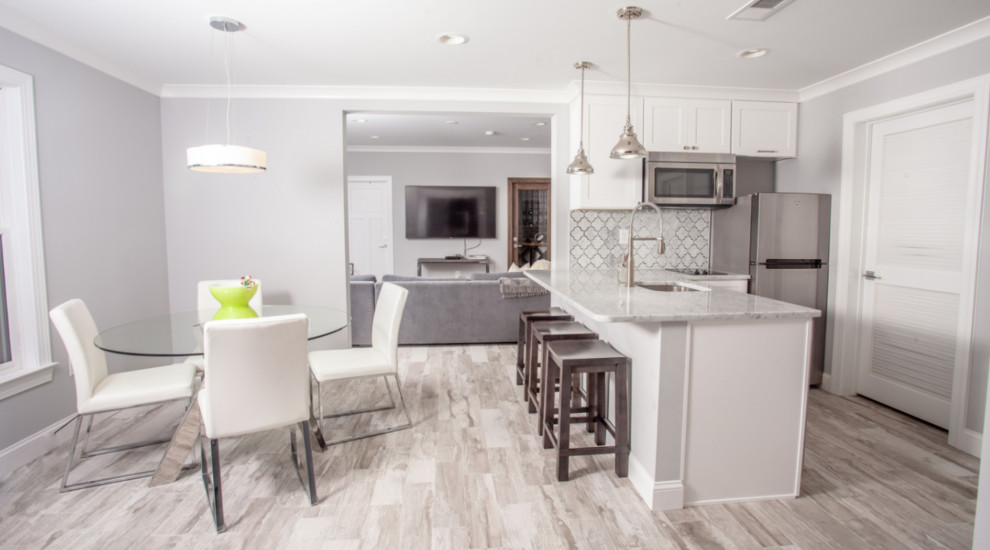 Inredning av ett klassiskt mellanstort vit vitt kök, med en undermonterad diskho, luckor med infälld panel, vita skåp, granitbänkskiva, vitt stänkskydd, stänkskydd i marmor, rostfria vitvaror, ljust trägolv, en halv köksö och grått golv