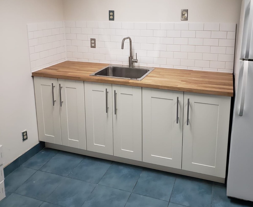 トロントにある小さな北欧スタイルのおしゃれなI型キッチン (ドロップインシンク、シェーカースタイル扉のキャビネット、白いキャビネット、木材カウンター、白いキッチンパネル、サブウェイタイルのキッチンパネル、白い調理設備、磁器タイルの床、アイランドなし、青い床、茶色いキッチンカウンター) の写真