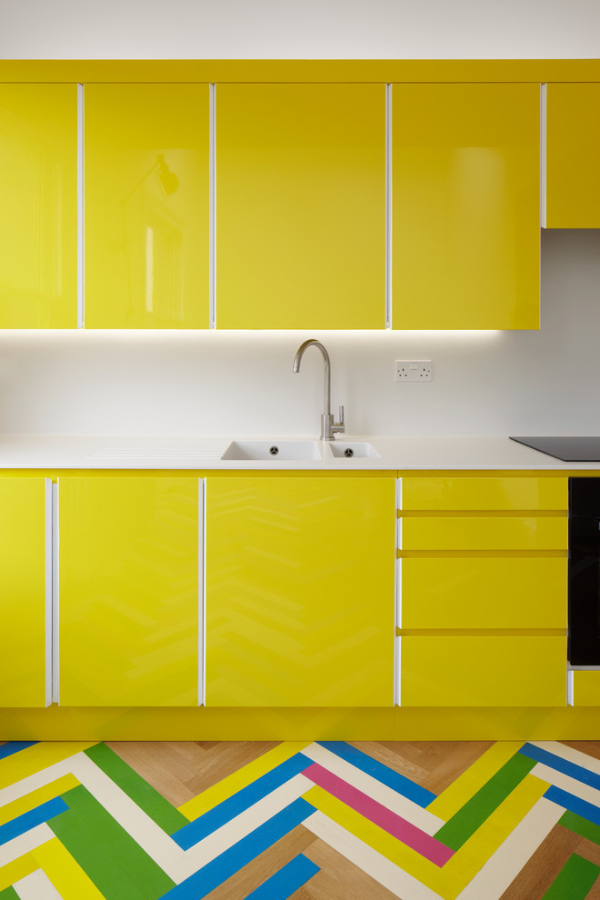 На фото: кухня в современном стиле с двойной мойкой, плоскими фасадами, желтыми фасадами, белым фартуком, деревянным полом и разноцветным полом с