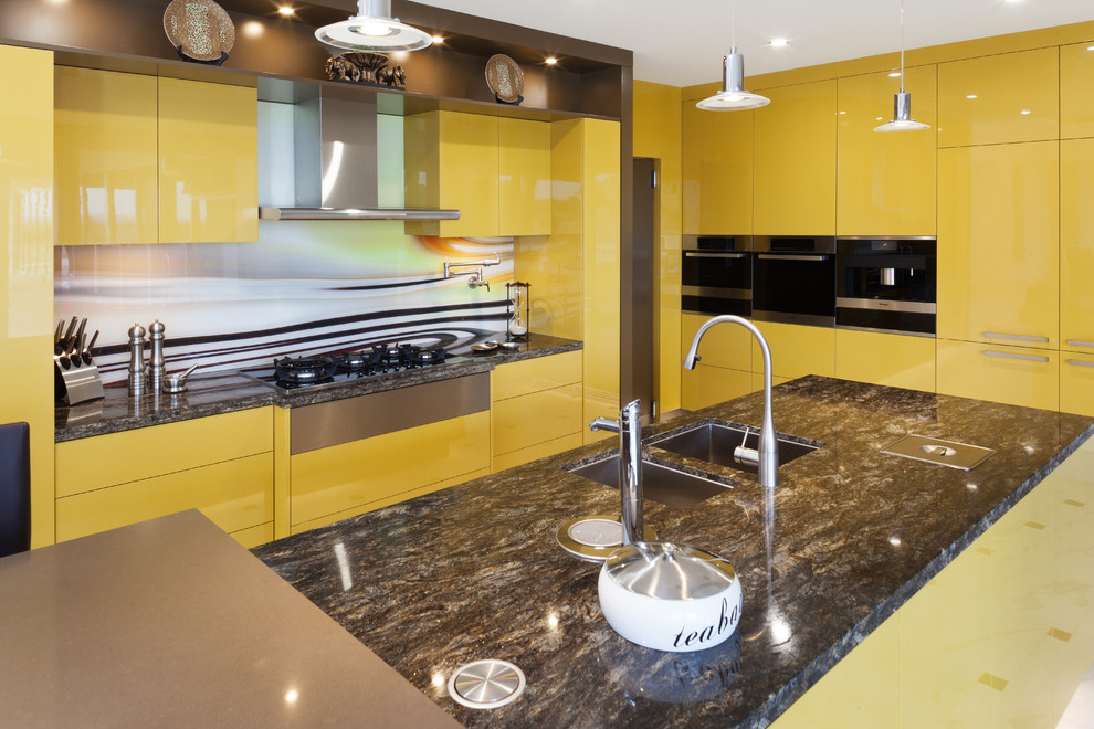 Foto di una cucina a L moderna con lavello sottopiano, ante lisce, ante gialle, top in granito, paraspruzzi multicolore, paraspruzzi con lastra di vetro, elettrodomestici in acciaio inossidabile, 2 o più isole e top multicolore