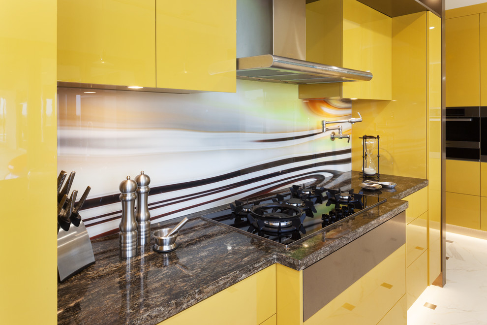 Immagine di una cucina moderna con ante lisce, ante gialle, top in granito, paraspruzzi multicolore, paraspruzzi con lastra di vetro, elettrodomestici in acciaio inossidabile e top marrone