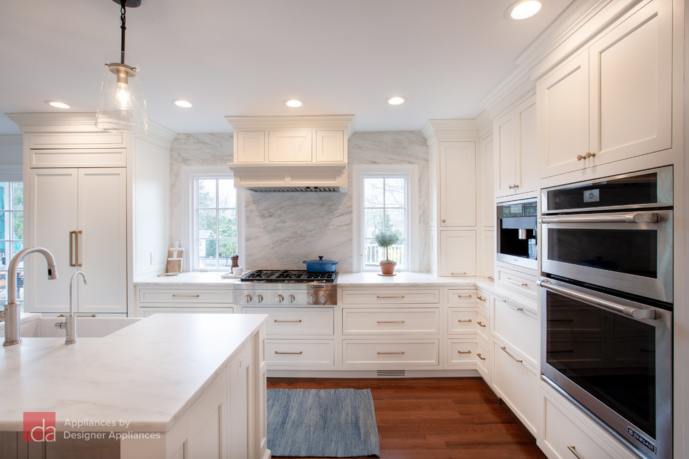 Inredning av ett klassiskt mellanstort vit vitt kök, med en rustik diskho, luckor med infälld panel, vita skåp, marmorbänkskiva, vitt stänkskydd, stänkskydd i marmor, rostfria vitvaror, mellanmörkt trägolv, en köksö och brunt golv