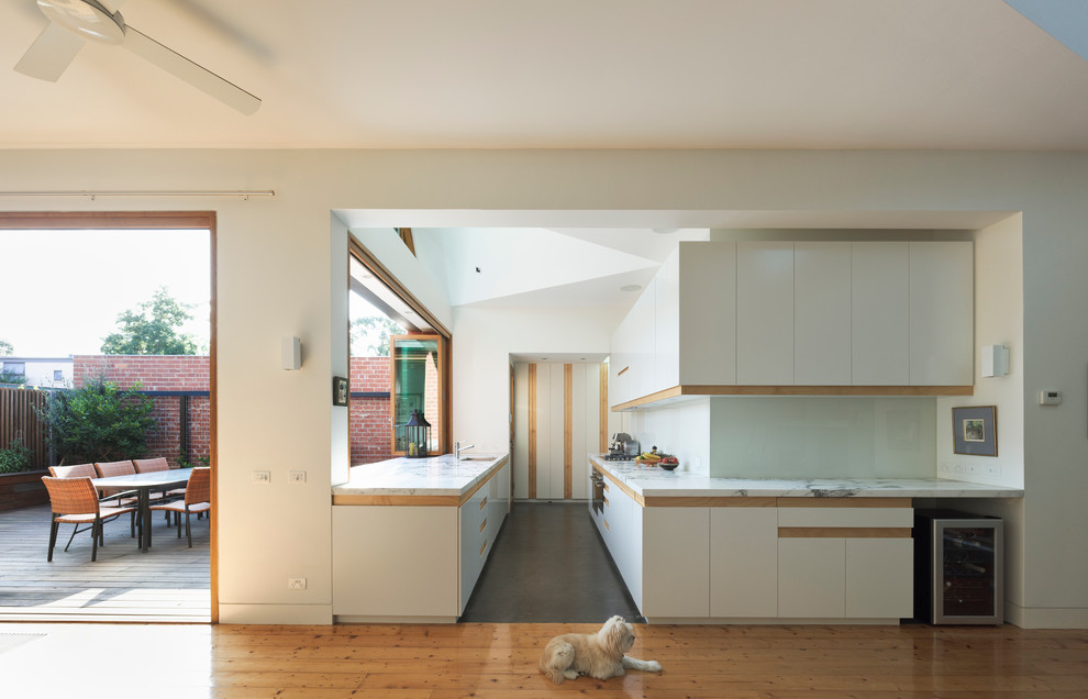 Photo of an expansive contemporary galley open plan kitchen in Melbourne with flat-panel cabinets, white cabinets, a submerged sink, marble worktops, white splashback, glass sheet splashback, stainless steel appliances, concrete flooring and no island.