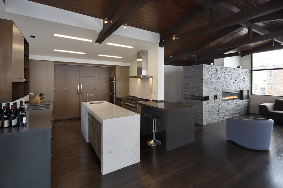 Bild på ett funkis kök, med rostfria vitvaror, en dubbel diskho, släta luckor, skåp i mörkt trä, marmorbänkskiva, vitt stänkskydd, stänkskydd i sten, mörkt trägolv och en köksö