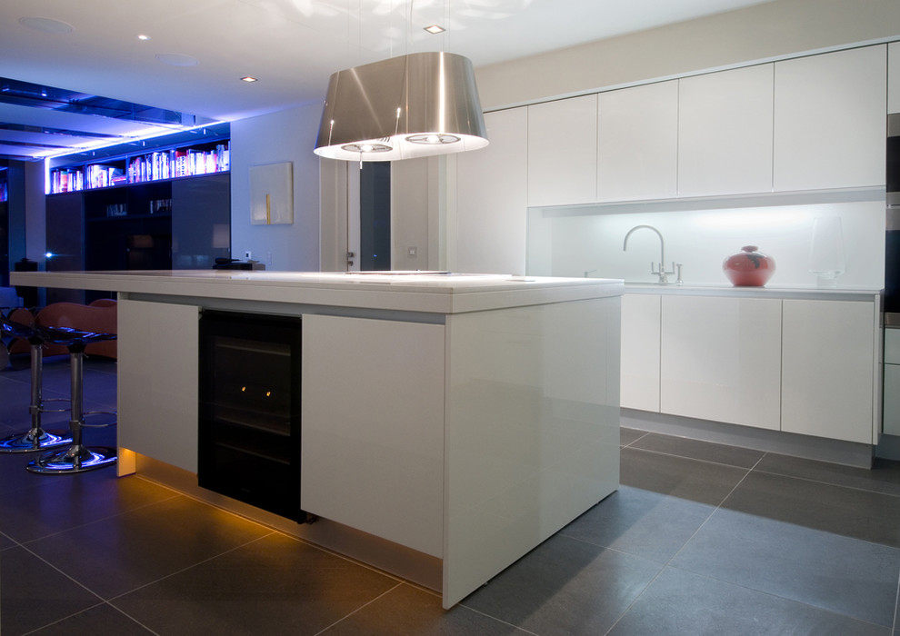 This is an example of a medium sized contemporary kitchen pantry in Dublin with a double-bowl sink, flat-panel cabinets, white cabinets, engineered stone countertops, white splashback, glass sheet splashback, black appliances, limestone flooring and an island.