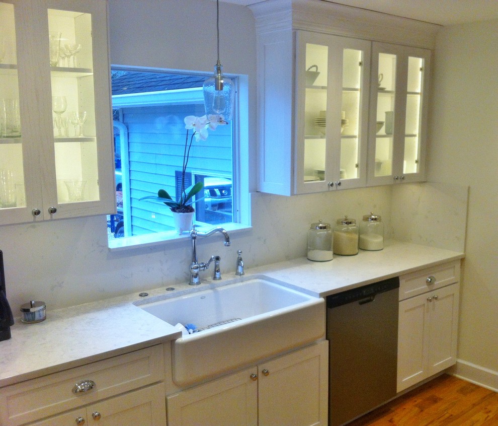 Example of a mid-sized transitional medium tone wood floor enclosed kitchen design in New Orleans with a farmhouse sink, shaker cabinets, white cabinets, quartz countertops, stainless steel appliances and no island