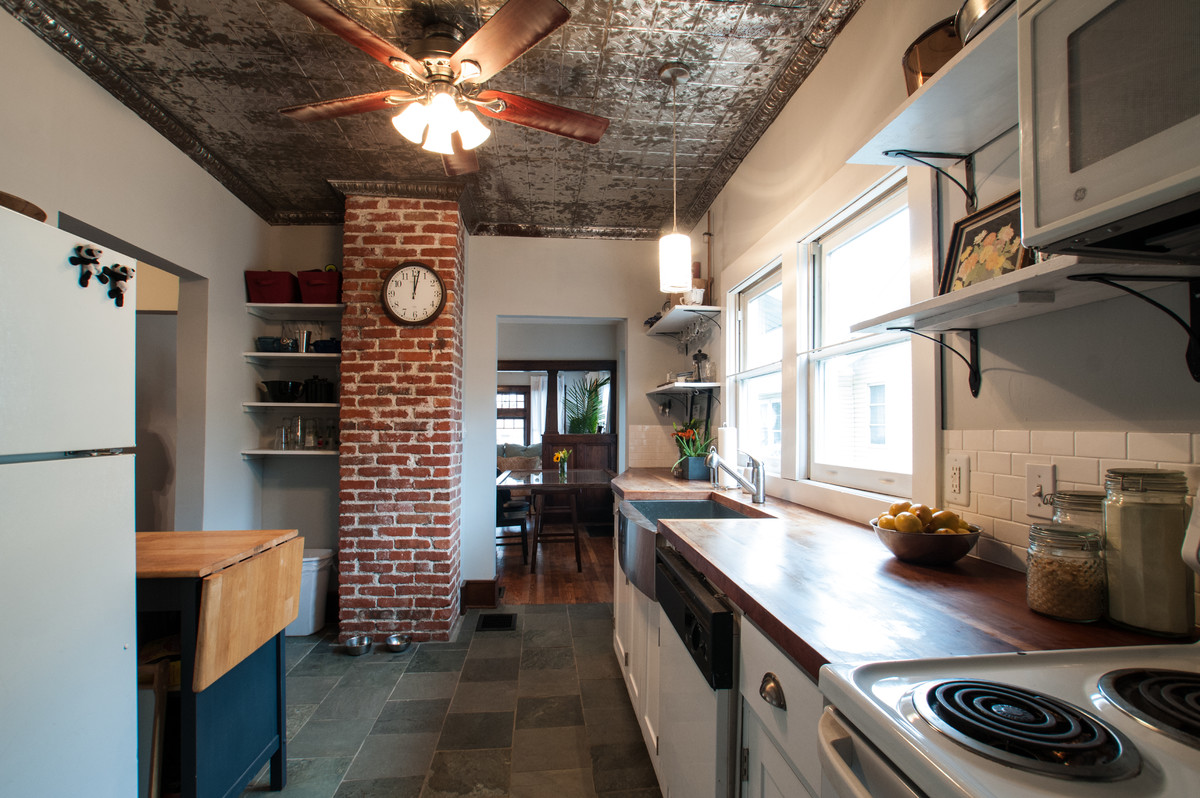 Bild på ett mellanstort parallellkök, med en rustik diskho, skåp i shakerstil, vita skåp, träbänkskiva, vitt stänkskydd, stänkskydd i keramik, vita vitvaror, skiffergolv, en köksö och grönt golv