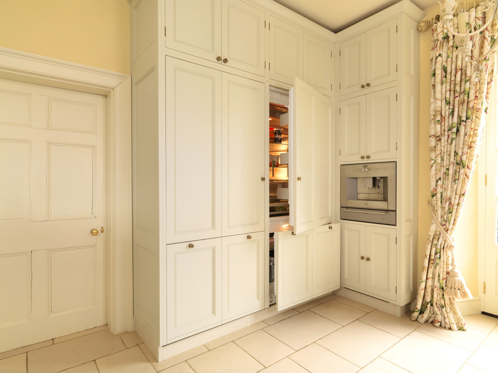 Modelo de cocina comedor clásica grande con fregadero integrado, armarios con paneles empotrados, puertas de armario blancas, encimera de granito, electrodomésticos con paneles, suelo de piedra caliza y una isla
