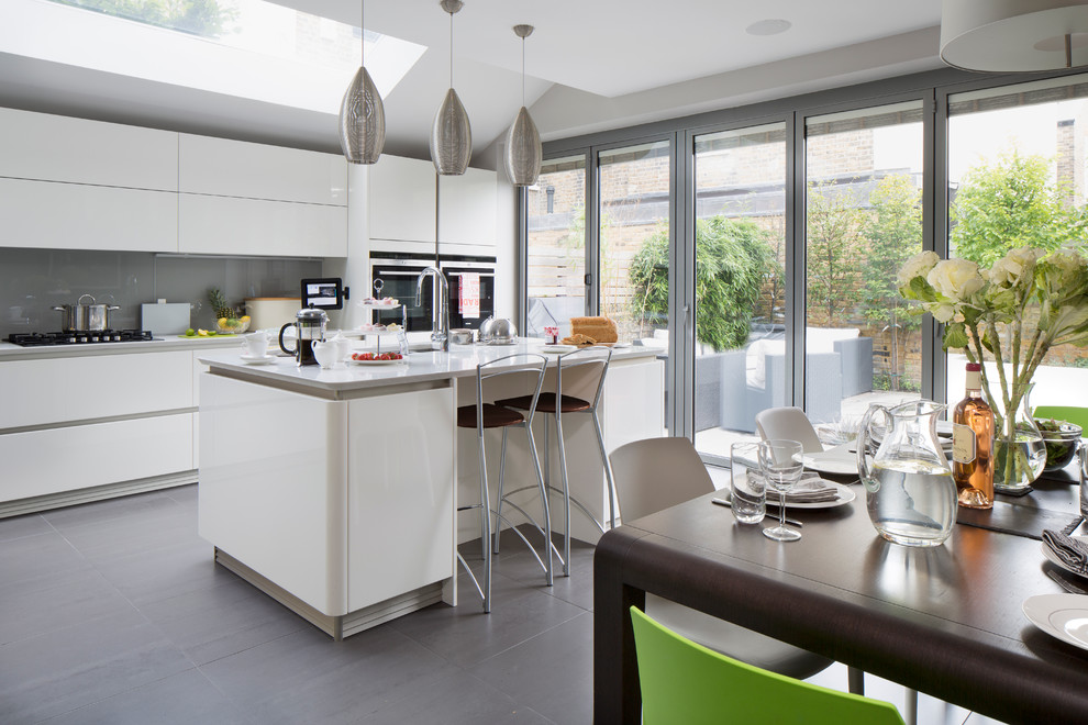 Trendy eat-in kitchen photo in London with flat-panel cabinets, white cabinets, gray backsplash, glass sheet backsplash and an island