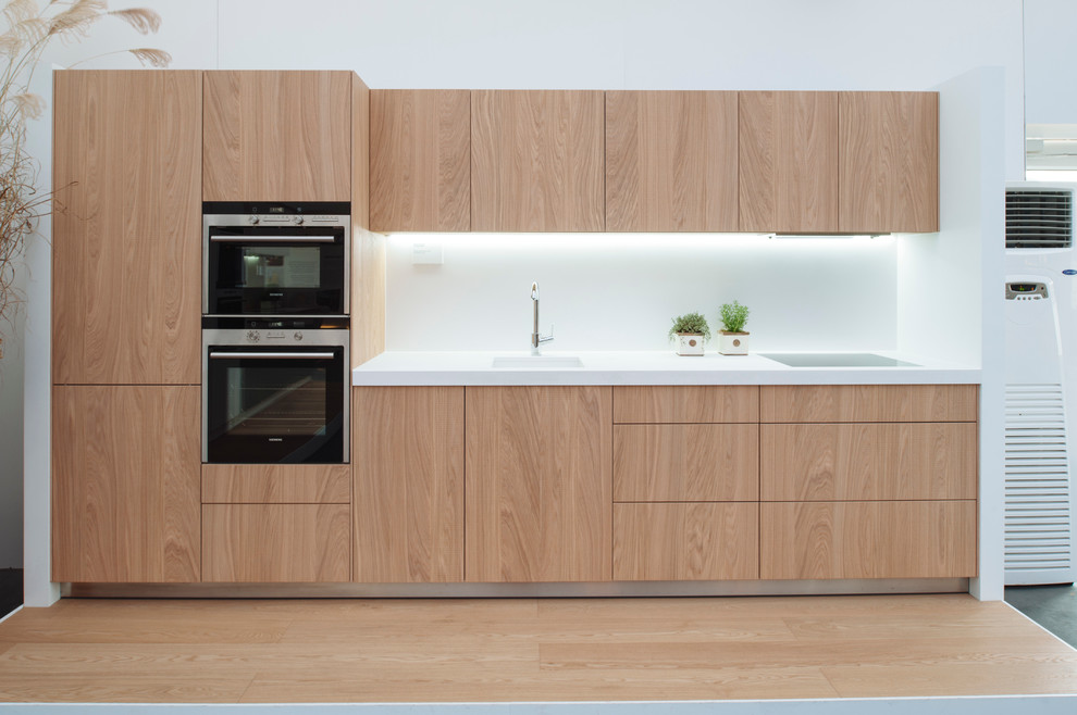 Cette image montre une cuisine linéaire et blanche et bois design en bois clair avec un évier 1 bac, un placard à porte plane et une crédence blanche.