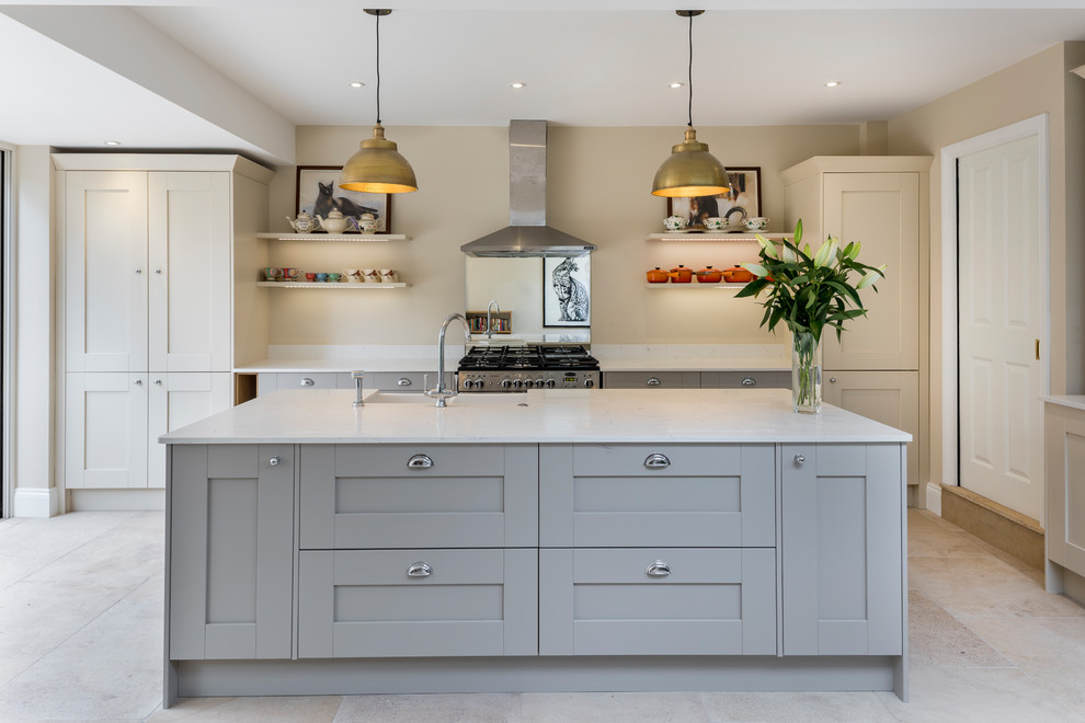 Example of a mid-sized transitional galley beige floor kitchen design in London with shaker cabinets, stainless steel appliances, an island, white countertops, a farmhouse sink and gray cabinets