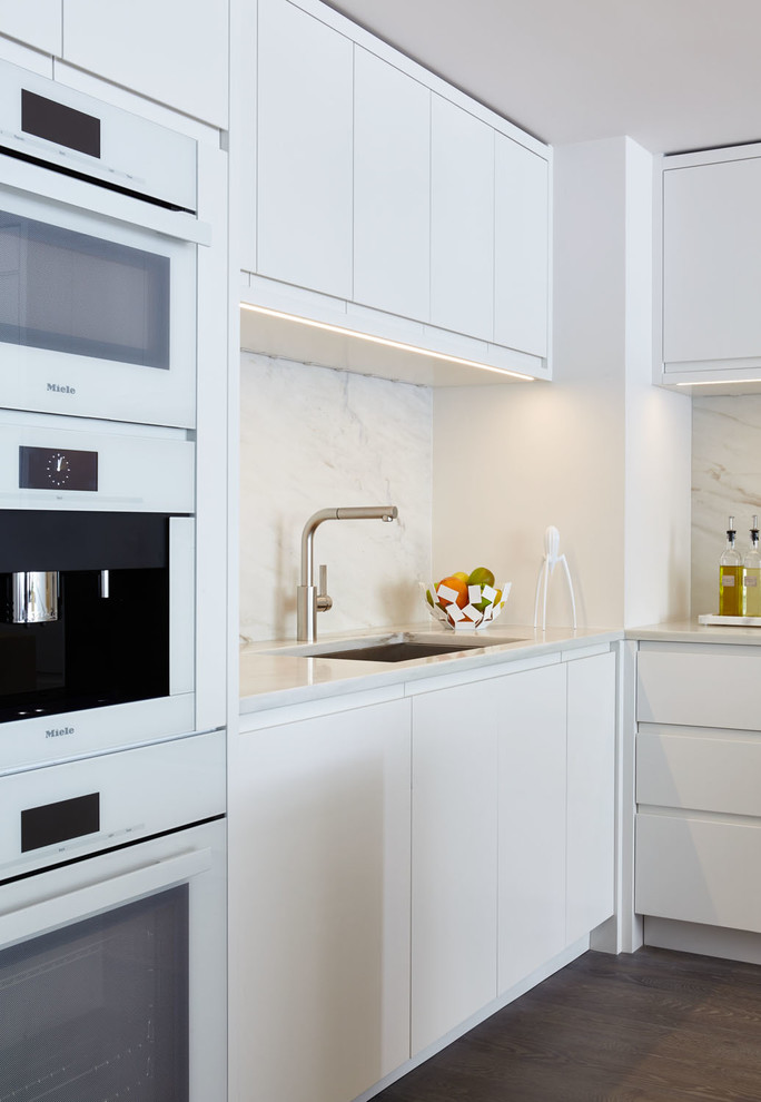 Idéer för ett mellanstort modernt flerfärgad kök, med en undermonterad diskho, släta luckor, vita skåp, marmorbänkskiva, flerfärgad stänkskydd, stänkskydd i sten, vita vitvaror, mellanmörkt trägolv, en köksö och brunt golv