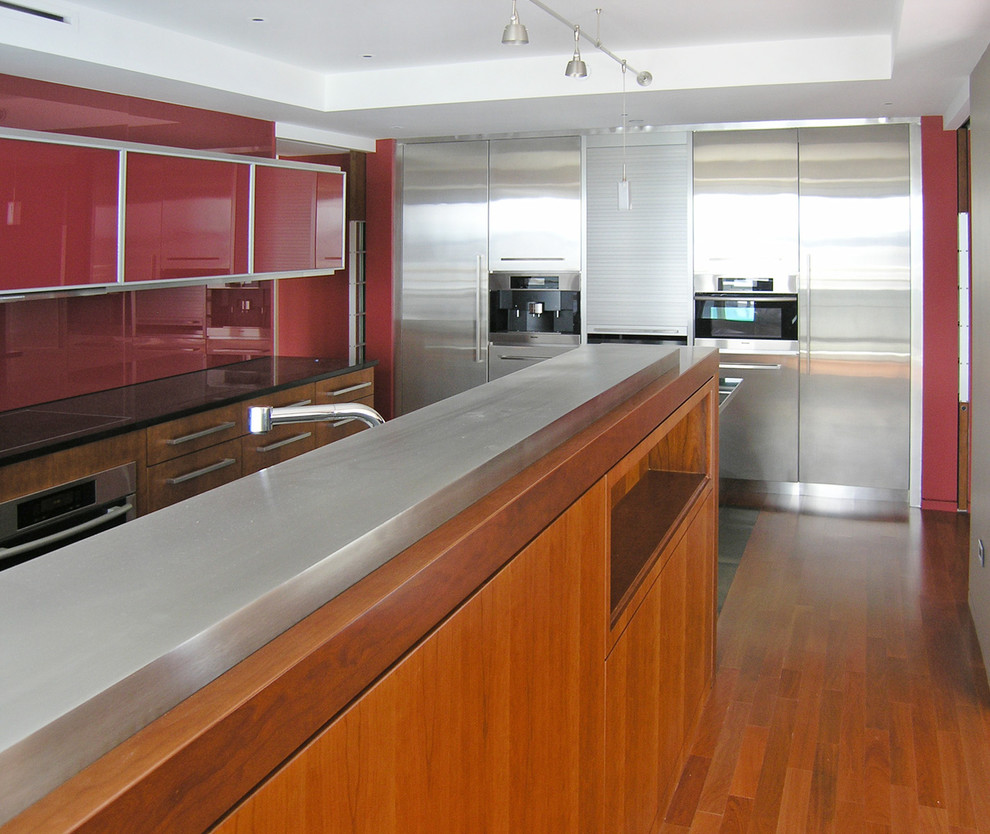 This is an example of a contemporary kitchen in Boston with flat-panel cabinets, stainless steel cabinets, red splashback and stainless steel appliances.