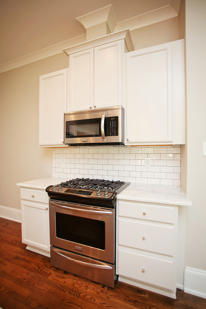 Große Klassische Küche in U-Form mit weißen Schränken, Küchenrückwand in Weiß, Rückwand aus Metrofliesen, Küchengeräten aus Edelstahl, braunem Holzboden und Kücheninsel in Charlotte