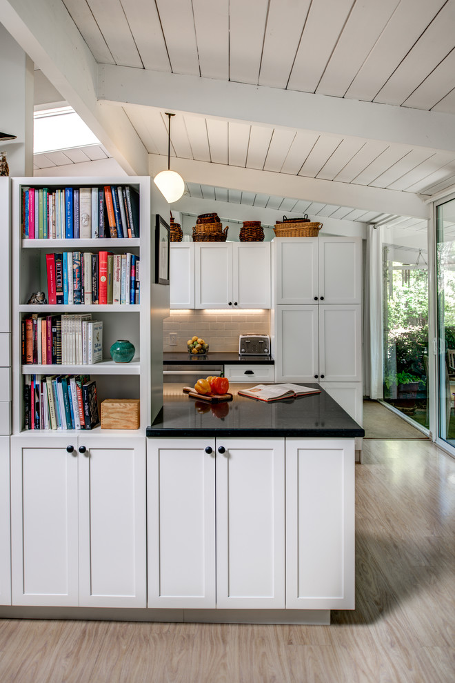 Small traditional galley kitchen pantry in San Francisco with a belfast sink, shaker cabinets, white cabinets, composite countertops, white splashback, porcelain splashback, stainless steel appliances, light hardwood flooring and an island.