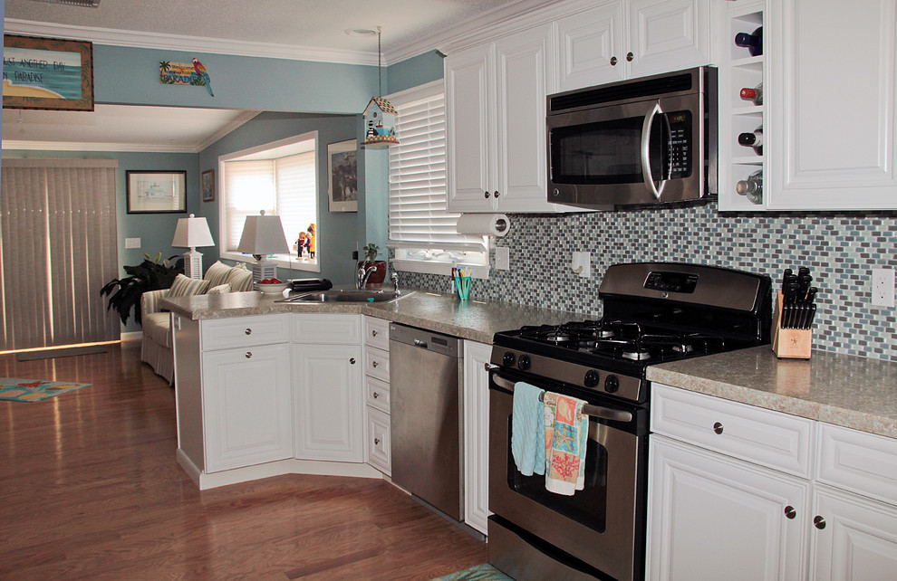 Exempel på ett mellanstort maritimt kök, med en nedsänkt diskho, luckor med upphöjd panel, vita skåp, laminatbänkskiva, blått stänkskydd, stänkskydd i glaskakel, rostfria vitvaror och mellanmörkt trägolv