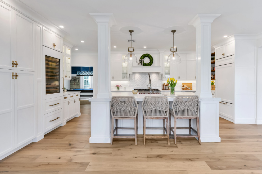 Transitional u-shaped light wood floor and beige floor kitchen photo in New York with a farmhouse sink, gray cabinets, white backsplash, paneled appliances, an island and white countertops