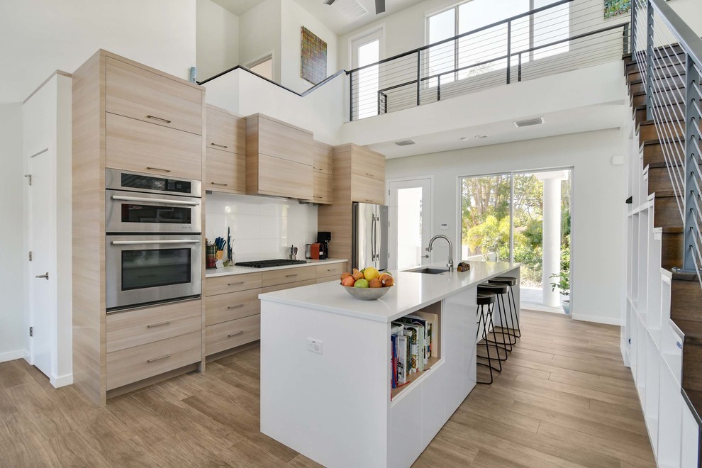 Design ideas for a contemporary galley kitchen in Tampa with a submerged sink, flat-panel cabinets, light wood cabinets, white splashback, stainless steel appliances, medium hardwood flooring, an island, brown floors and white worktops.